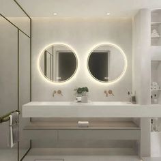 a white bathroom with two round mirrors above the sinks and lights on the wall behind it