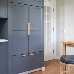 an empty kitchen with blue cabinets and stools next to a counter top, in front of a white door