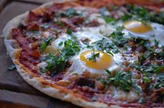 an egg and bacon pizza on a wooden board with parsley sprinkled around the edges