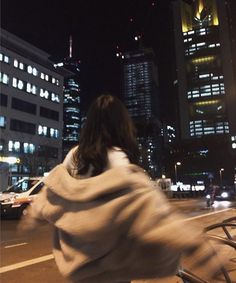 a woman is riding her bike down the street at night with city lights in the background