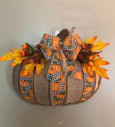 a decorative pumpkin hanging from the wall with fall leaves and plaid ribbon on it's head