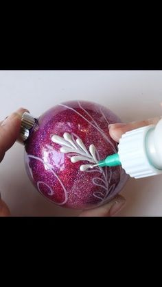 someone is decorating an ornament with purple and white paint on the ball