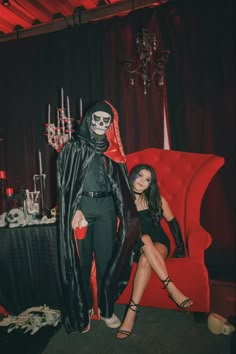 two women dressed up in halloween costumes posing for a photo next to a red chair