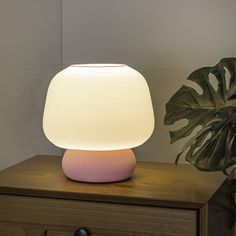 a pink lamp sitting on top of a wooden table next to a potted plant