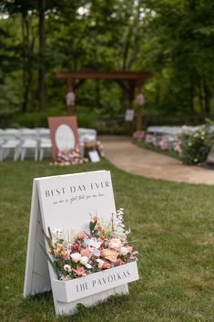 a sign with flowers on it sitting in the middle of a grass covered park area