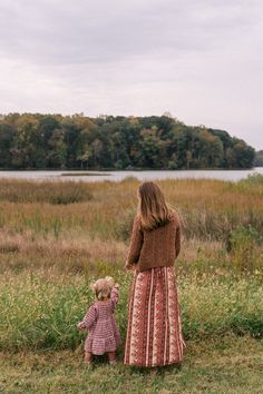 a mother and her child are standing in the grass looking out at the water on a cloudy day