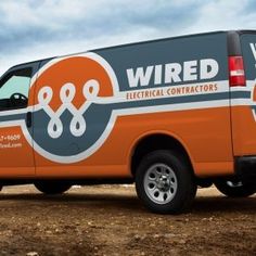 an orange and black van parked on dirt field next to rocks with cloudy sky in background