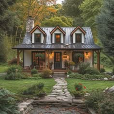 a small house with a metal roof and stone walkway leading to the front door is surrounded by greenery