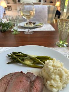 a white plate topped with meat, mashed potatoes and asparagus next to a glass of wine