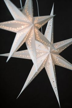 three white paper stars hanging from strings on a black background, with lights in the middle