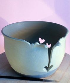 a white bowl with two hearts in the center on a wooden table next to a pen