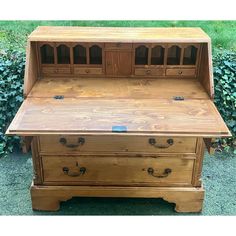 a wooden desk with two drawers and one drawer on the top, in front of some bushes