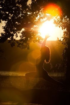 the woman is doing yoga outside in the sun light, with her arms up to the sky