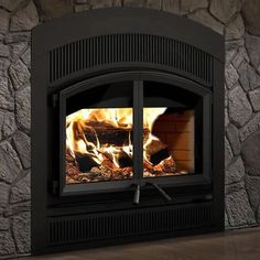 a fire burning in a fireplace with rocks on the wall and wood flooring around it