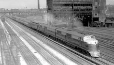 a black and white photo of a train coming down the tracks in an industrial area