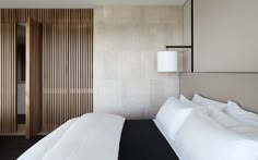 a bed with white sheets and pillows next to a wooden wall in a hotel room