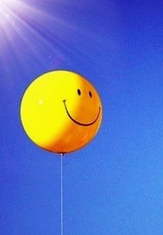 a yellow smiley face balloon flying in the sky with sun shining on it's side