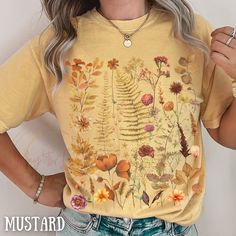 "This botanical shirt with autumn inspired wildflower meadows pressed flowers captures the essence of nature's beauty and makes a splendid addition to your wardrobe. This shirt is not just a wardrobe staple; it's a heartfelt gesture for any occasion. Be it Mother's Day or a spontaneous surprise, it's a thoughtful gift that speaks to her love for all things floral and natural. Elevate her style and express your appreciation with this exquisite wildflower tee, a symbol of beauty, serenity, and the Fall Yellow Shirt With Floral Print, Floral Print Crew Neck Shirt For Fall, Fall Floral Print Crew Neck Shirt, Fall Floral Print T-shirt, Flower Minimalist, Floral Clothing, Wildflower Field, Autumn Inspired, Cottagecore Style