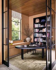 a room with a table, bookshelf and vase on the floor in front of a window