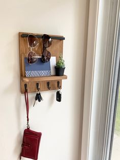 a wooden shelf with sunglasses, wallet and purse hanging on the wall next to a window