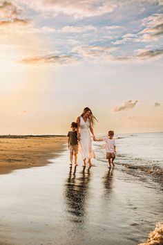 a woman and two children are walking on the beach at sunset with their arms around each other