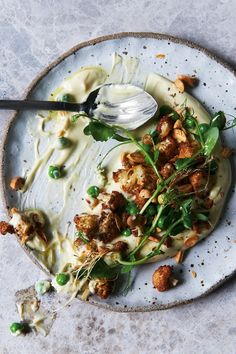 a white plate topped with food next to a silver spoon and sauce on top of it