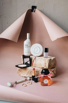 an assortment of personal care items displayed on a pink surface with a triangular shaped object in the background