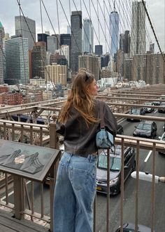 a woman standing on the side of a bridge looking at cars and buildings in the distance