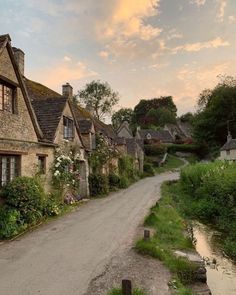 an old stone house with flowers growing on it's side and a river running through the middle