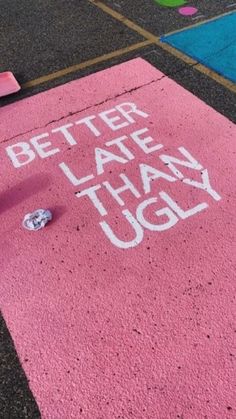 a skateboard laying on the ground next to a pink sign that says better late than ugly