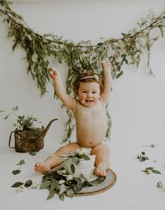 a baby sitting on the floor with greenery around her