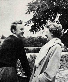 an old black and white photo of two people standing next to each other in front of a tree