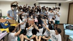 a group of people wearing masks and sitting in front of a classroom full of students