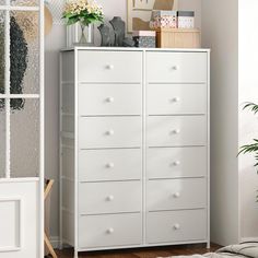 a white chest of drawers next to a window in a room with plants and pictures on the wall