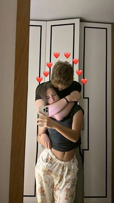 two people hugging each other with hearts on the wall behind them and one person holding a cell phone