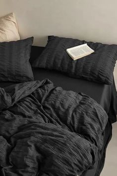 a bed with black sheets and pillows on top of it next to a white wall