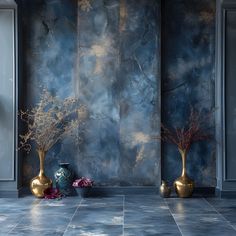 two vases with flowers are sitting on the floor in front of a blue wall