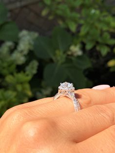 a woman's hand holding an engagement ring in front of some plants and bushes