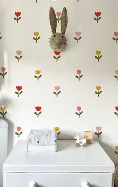 a white dresser sitting next to a wall with flowers and a bunny head on it