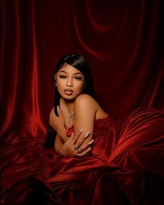 a woman laying on top of a red bed covered in sheets and pillows with her arms crossed