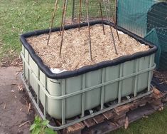 a large container filled with dirt sitting on top of a grass covered ground next to a fence