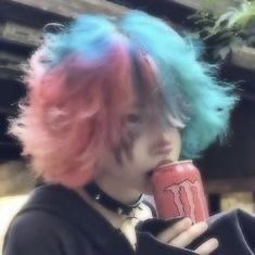 a woman with pink and blue hair drinking from a can