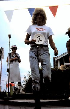 a woman holding a white frisbee while standing on top of a stage with other people in the background