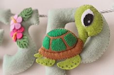 two felt turtle ornaments hanging from a string on a white surface with pink and green flowers