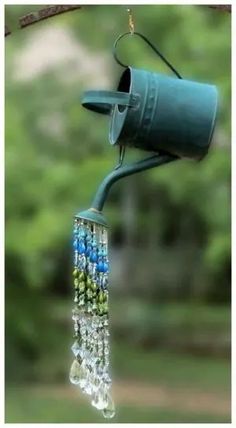 a blue bird feeder hanging from a tree branch with beads and chains attached to it