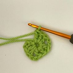 an orange crochet hook with green yarn next to it on a white surface