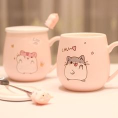 two mugs with cartoon characters on them sitting on a table next to a spoon