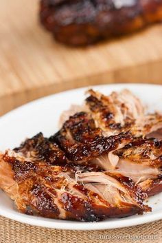 some meat is on a white plate and next to another food item that has been placed on a wooden table