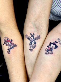 two people with mickey and minnie mouse tattoos on their arms, both holding each other's hands