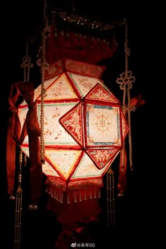 a red and white light hanging from a ceiling in the dark with chains attached to it